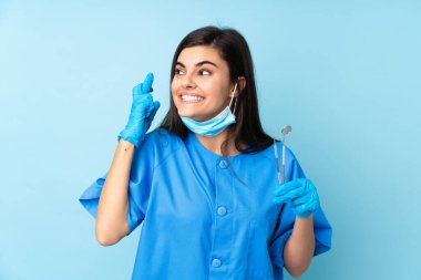 İzole edilmiş mavi arka plan üzerinde aletleri tutan genç bir dişçi.