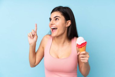 İzole edilmiş mavi arka planda kornet dondurması tutan genç bir kadın çözümü bulmak için parmağını kaldırıyor.