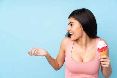 Kornet dondurması tutan genç bir kadın izole edilmiş mavi arka planda, şaşırmış bir yüz ifadesi var.