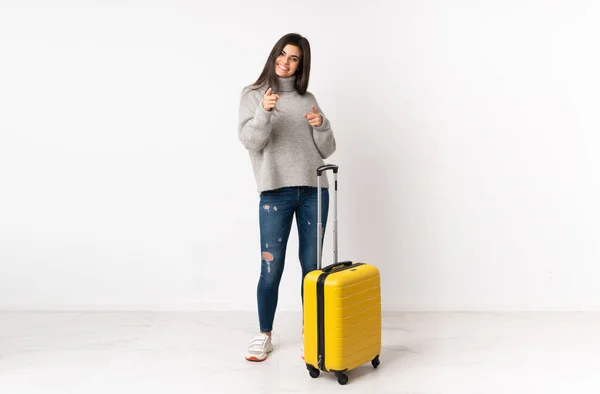 白い壁の上にスーツケースを持つ旅行者の女性の完全な長さ体指であなたを指します — ストック写真