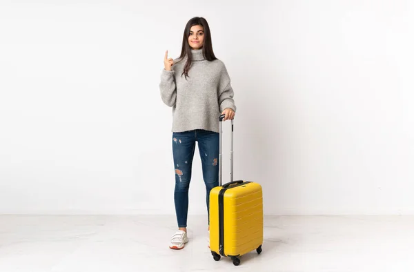 一个全身上下都是一个旅行的女人 她背着一个手提箱 穿过孤立的白墙 用食指指向一个绝妙的主意 — 图库照片