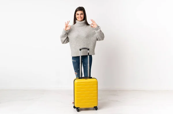 一个带着手提箱的女旅行家的全身上下 隔着一堵白色的墙 用手指显示出一个还好的标志 — 图库照片