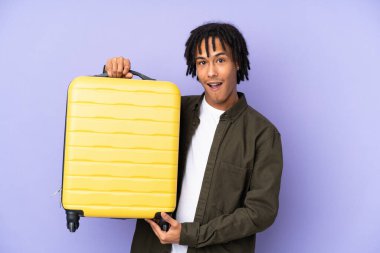 Genç Afro-Amerikan bir adam, mor arka planda izole edilmiş seyahat valiziyle tatilde.