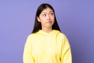 Genç Asyalı kadın mor arka planda izole edilmiş ve yukarı bakıyor.