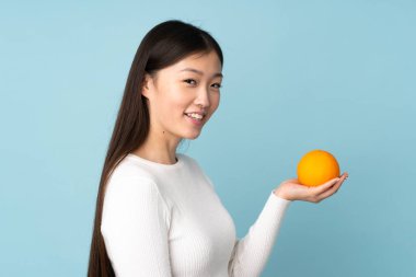 İzole edilmiş mavi arka planda portakal tutan genç Asyalı kadın.