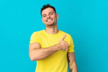 Beyaz tenli yakışıklı adam mavi arka planda izole edilmiş bir şekilde baş parmak işareti yapıyor.