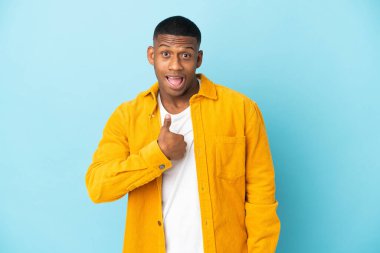 Mavi arka planda yalıtılmış genç latin adam, şaşırmış yüz ifadesi ile