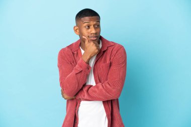 Genç latin adam mavi arka planda izole edilmiş, yana bakıyor ve gülümsüyor.