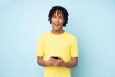 Genç Afrikalı Amerikalı bir adam mavi arka planda izole edilmiş, şaşırmış ve bir mesaj gönderiyor.