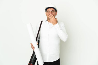 Miğferli ve elinde planları olan genç bir mimar beyaz arka planda izole edilmiş mutlu ve gülümseyen ağızlarını eliyle kapatıyor.