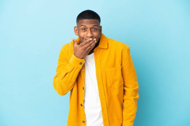 Mavi arka planda izole edilmiş genç Latin adam mutlu ve gülümsüyor.