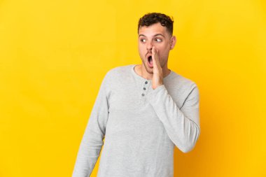 Beyaz tenli yakışıklı adam sarı arka planda izole edilmiş. Yan tarafa bakarken sürpriz bir jest yapıyor.