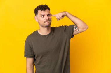 Sarı arka planda izole edilmiş beyaz, yakışıklı genç bir adam. Çılgınlık hareketi yapıyor. Parmağını kafaya koyuyor.