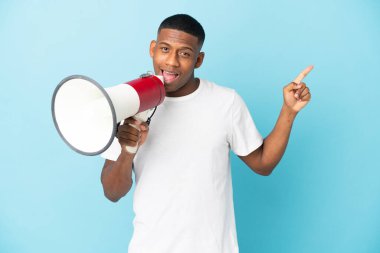 Mavi arka planda izole edilmiş genç bir latin adam megafonla bağırıyor ve işaret ediyor.