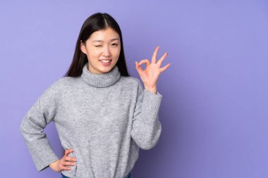 İzole edilmiş arka planda genç Asyalı kadın parmaklarıyla işaret veriyor.