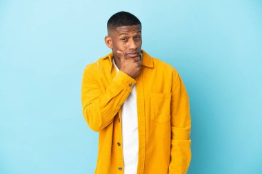 Mavi arka planda izole edilmiş genç latin adamın şüpheleri var.