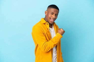 Mavi arka planda izole edilmiş genç latin adam zaferi kutluyor.