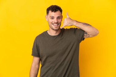 Sarı arka planda izole edilmiş beyaz, yakışıklı genç bir adam telefon jesti yapıyor. Bana geri dönüş işareti ver.