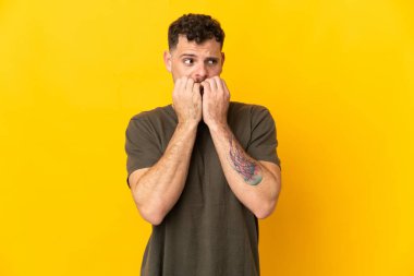 Beyaz tenli yakışıklı adam sarı arka planda izole edilmiş gergin ve korkmuş halde elleriyle suni teneffüs yapıyor.