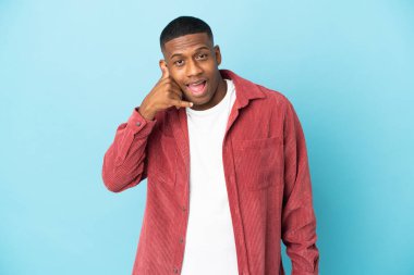 Mavi arka planda izole edilmiş genç latin adam telefon jesti yapıyor. Bana geri dönüş işareti ver.