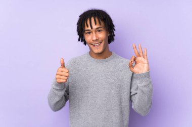 Mor arka planda izole edilmiş genç Afro-Amerikalı adam işaret ve baş parmak hareketi gösteriyor.
