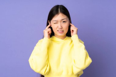 Mor arka planda izole edilmiş genç Asyalı kadın hayal kırıklığına uğramış ve kulaklarını kapatmış.