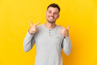 Sarı arka planda izole edilmiş beyaz, yakışıklı genç bir adam baş parmak işareti yapıyor.