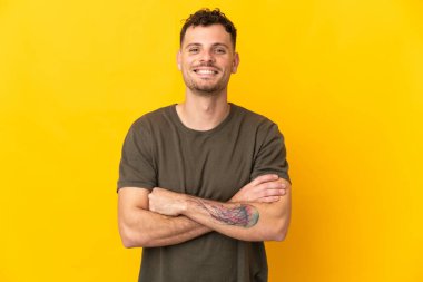 Sarı arka planda izole edilmiş beyaz, yakışıklı genç bir adam kollarını ön cephede kavuşturuyor.