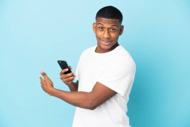 Genç latin adam mavi arka planda cep telefonu kullanarak izole edilmiş.