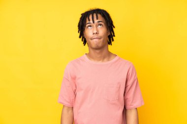 Genç Afrikalı Amerikalı adam sarı arka planda izole edilmiş ve yukarı bakıyor.