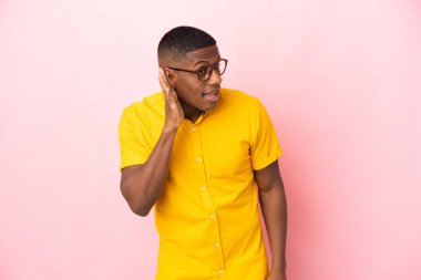 Pembe arka planda izole edilmiş genç latin adam. Kulağına elini sürerek bir şeyler dinliyor.