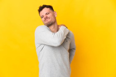 Beyaz tenli yakışıklı, sarı arka planda izole edilmiş, omuz ağrısından muzdarip, çaba sarf ettiği için.