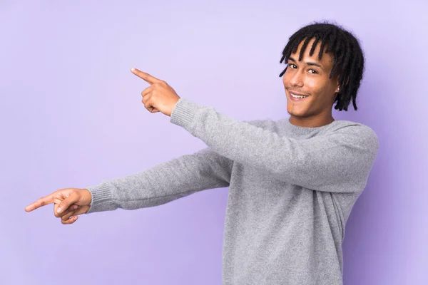 年轻的非洲裔美国人被紫色背景隔离 手指指向侧面并展示了一种产品 — 图库照片
