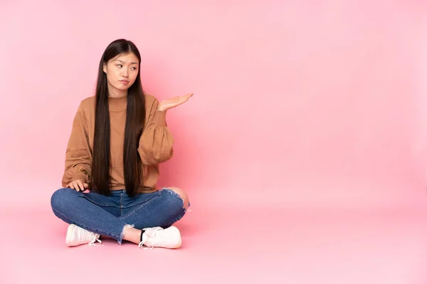 Jovem Mulher Asiática Sentado Chão Isolado Fundo Rosa Segurando Copyspace — Fotografia de Stock