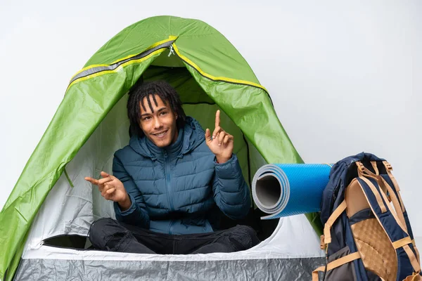 Young african american man inside a camping green tent pointing finger to the laterals and happy