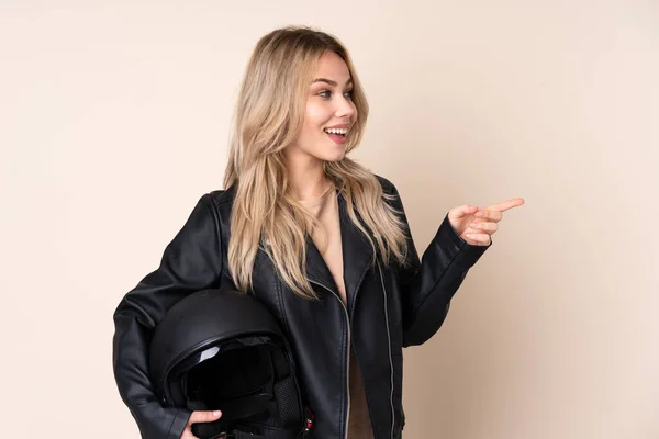 ロシアの女の子とともにオートバイのヘルメット隔離された上ベージュの背景指差し指に側面と製品を提示 — ストック写真