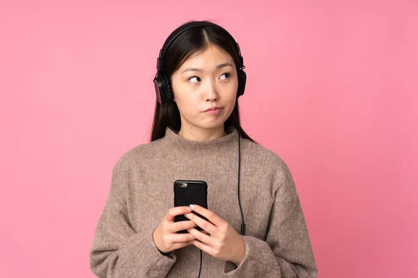 Νεαρή Ασιάτισσα Απομονωμένη Ροζ Φόντο Ακούγοντας Μουσική Κινητό Και Σκεπτόμενη — Φωτογραφία Αρχείου