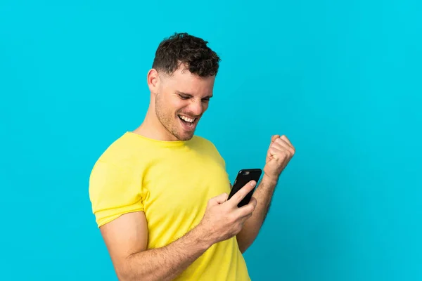 Young Caucasian Handsome Man Isolated Blue Background Phone Victory Position — Stock Photo, Image