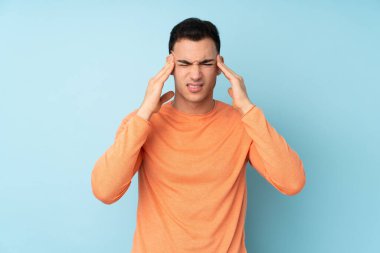 Kafkasyalı yakışıklı genç adam mavi arka planda başağrısı ile izole edilmiş.