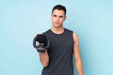 Mavi arka planda izole edilmiş genç bir sporcu halter olarak ağırlık kaldırıyor.