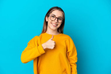 Mavi arka planda izole edilmiş beyaz bir kadın baş parmak işareti yapıyor.