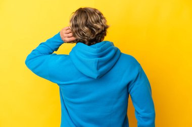 Sarışın yakışıklı adam sarı arka planda izole edilmiş ve düşünüyor.