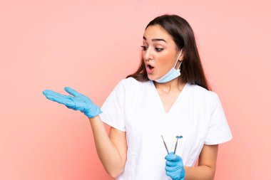 Pembe arka planda izole edilmiş aletleri tutan kadın diş hekimi avucunun içinde görsel alan tutuyor.