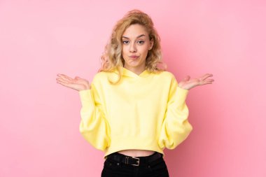 Pembe arka planda izole edilmiş sweatshirt giyen genç sarışın kadın ellerini kaldırırken şüpheye düşüyor.