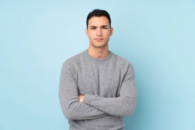 Mavi arka planda izole edilmiş, kollarını kavuşturan beyaz, yakışıklı genç bir adam.