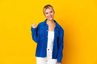 Sarı arka planda izole edilmiş genç bir Rus kadın bir ürün sunmak için kenarı işaret ediyor.
