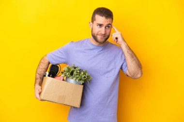 Genç Kafkasyalı, sarı arka planda izole edilmiş şeylerle dolu bir kutuyu seçerken bir hamle yapıyor. Şüpheleri var ve düşünüyor.