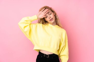 Tişört giyen genç sarışın kadın pembe arka planda izole edilmiş, yorgun ve hasta bir ifadeyle.