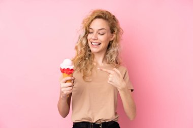 Pembe arka planda izole edilmiş kornet dondurması tutan genç sarışın kadın.