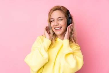 Pembe arka planda izole edilmiş sweatshirt giyen genç sarışın kadın müzik dinliyor ve şarkı söylüyor.